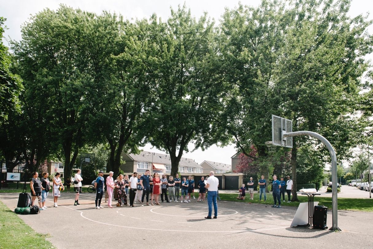 een groep mensen buiten op een basketbalveld wordt toegsproken